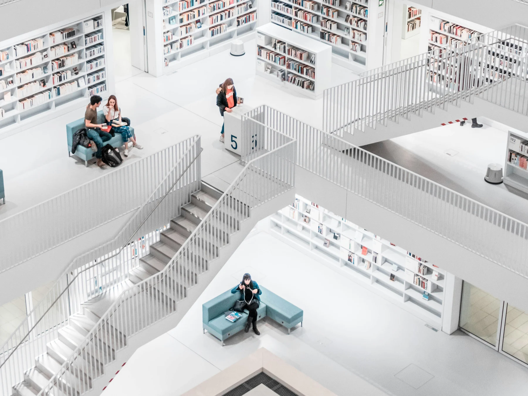 Lower floors of the same library, readers on teal sofas among white staircases