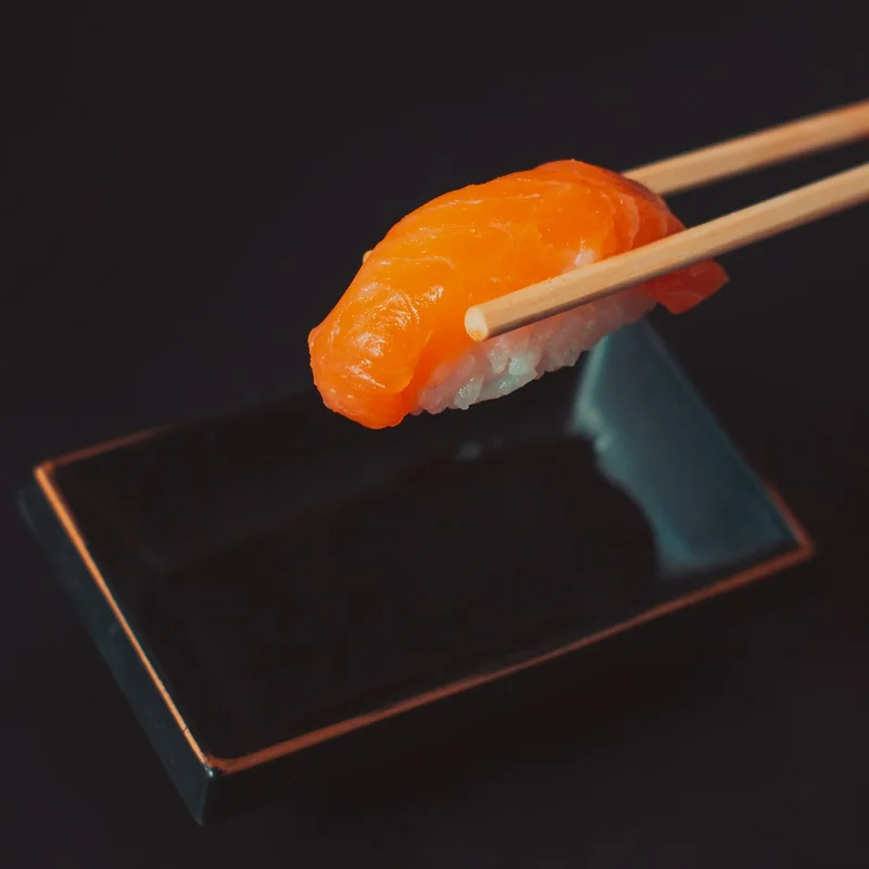 Salmon nigiri held in chopsticks over a black tray